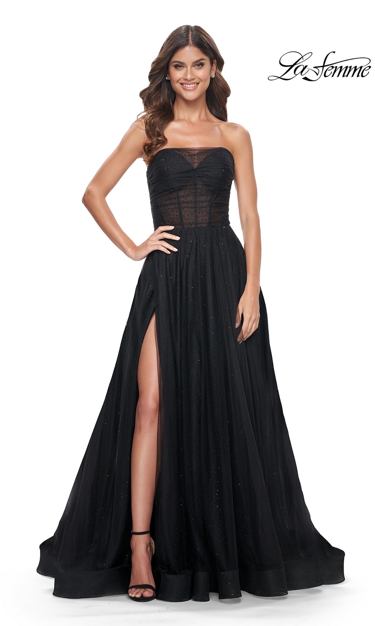 Model wearing the La Femme Long Black Strapless Prom Ball Gown 32029, featuring a sheer bodice, high slit, and subtle sparkle accents, standing with one hand on her hip.